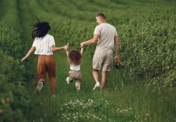 A joyful family strolls through a lush green field, enjoying quality time together.